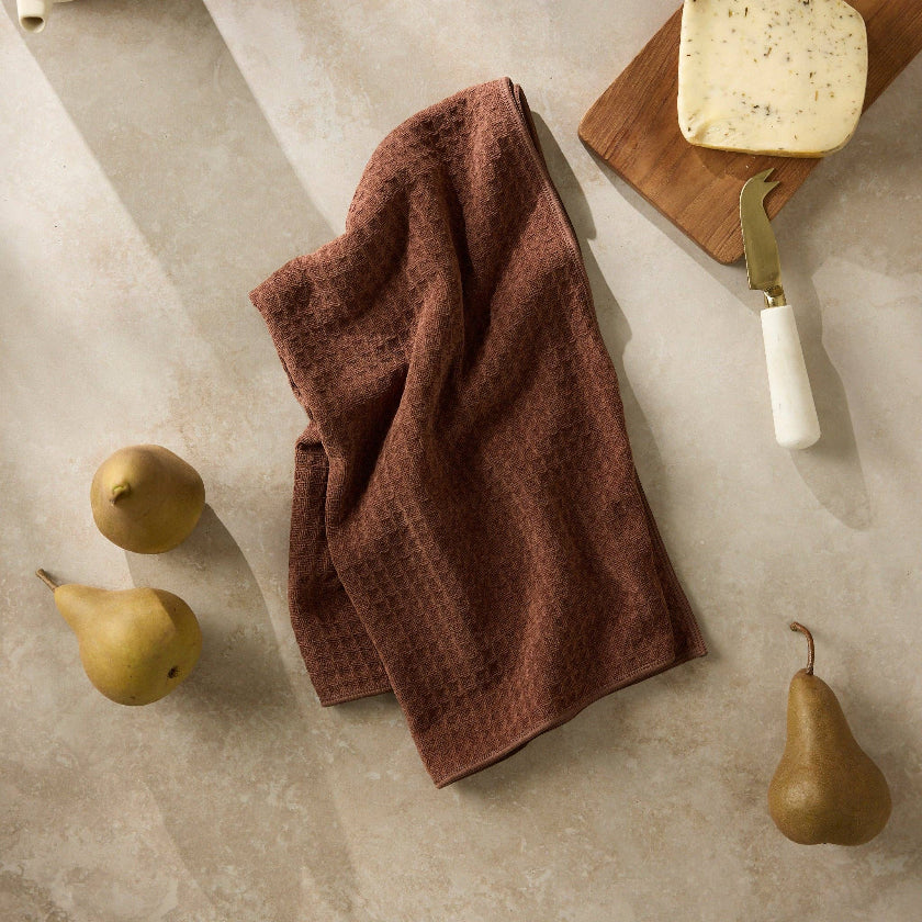 Brown towel on a stone surface with pears and a cutting board.