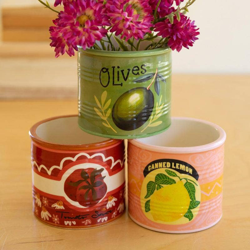 Three repurposed can vases with floral arrangements on a wooden surface.