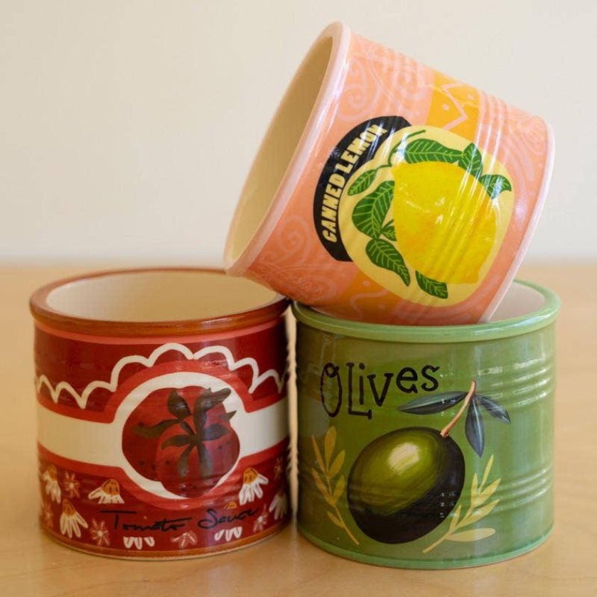 Three decorative tins with fruit and olive designs on a wooden surface.